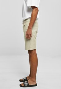 Pantalones cortos beige de mezcla de algodón con corte ajustado, bolsillos laterales y cierre de botón. Combinados con sandalias negras tipo chanclas con letras blancas.