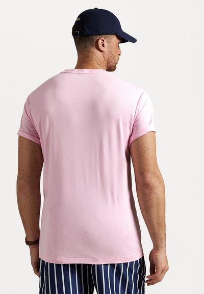 Rožinė trumpa rankovė t-shirt su apvaliu kaklu ir sukabintais rankovėmis, pagaminta iš minkštos medžiagos. Nešiojama su dryžuotais mėlynais ir baltais šortais.