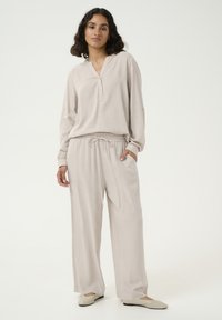 Haut beige léger à manches longues avec un col en V et une patte de boutonnage, associé à un pantalon ample à cordon de serrage dans une teinte assortie.