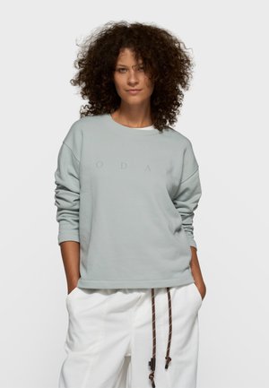 Lichtgrijze trui met een ronde hals, voorzien van een getextureerde afwerking en een subtiele "TODAY"-print. Gecombineerd met witte broek en bruine trekkoorden.