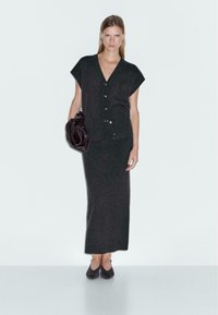 Ensemble en tricot gris foncé composé d'un haut à manches courtes et bouton et d'une jupe longue assortie. Les accessoires comprennent un sac à main sombre.