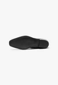 Suela de zapato de cuero negro con una forma estilizada y puntiaguda. Textura suave y características de tracción mínimas, diseñado para vestimenta formal.