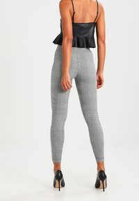 Svart konstläder peplumtoppar i kombination med figurnära grå hounds-tooth leggings. Outfitet har höga klackar i en svart och beige färgskala.