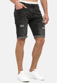 Zwarte denim short met opgerolde broekspijpen, voorzien van versleten plekken en zakken. Het combineren met witte sneakers maakt de look compleet.