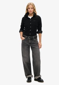 Sort kordfløjlsskjorte med knaplukning og oprullede ærmer, parret med vide grå denimjeans og sorte sko.