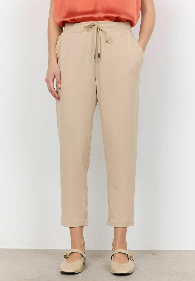 Beige tapering broek met een trekkoord in de taille, zijzakken en textuuraccenten aan de zijkanten. Gemaakt van een gladde stof, eindigend boven de enkel.