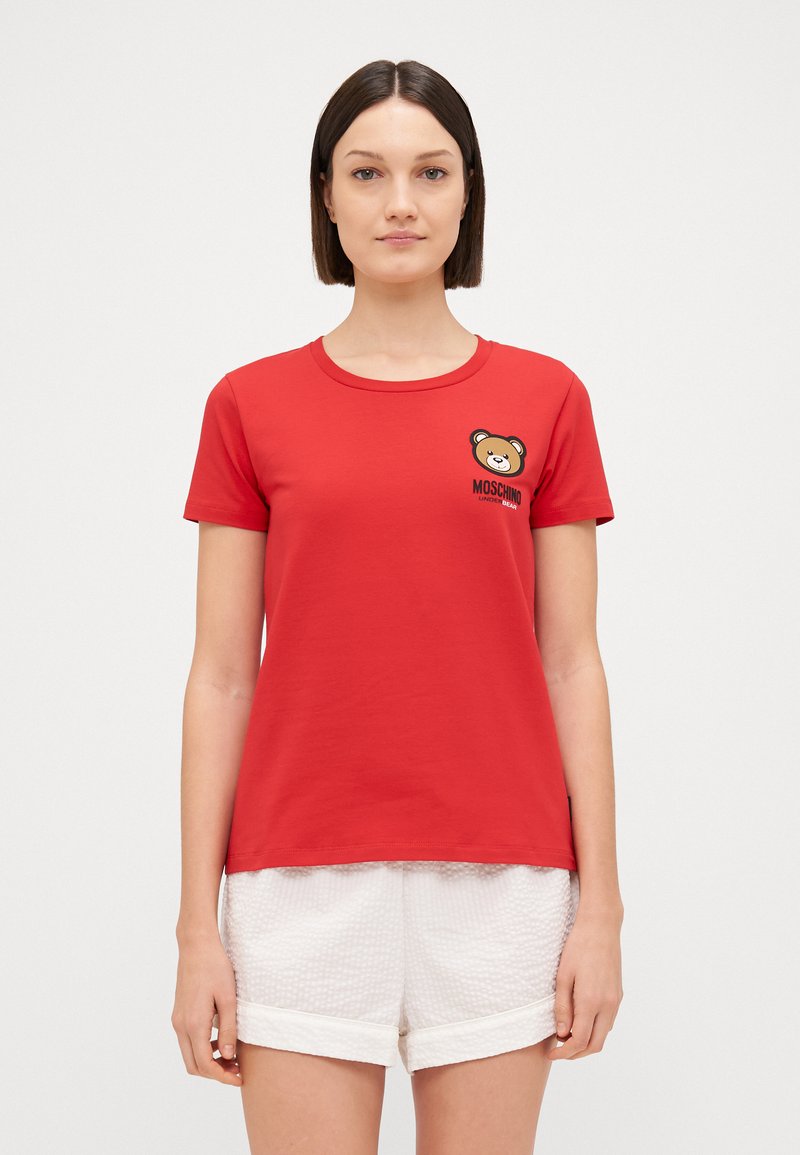 Κόκκινο βαμβακερό μπλουζάκι με κοντά μανίκια, στρογγυλή λαιμόκοψη και γραφικό με αρκούδα και το κείμενο "Moschino Under Bear" στην αριστερή πλευρά του στήθους.