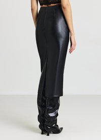 Gonna in pelle nera con spacco alto, trama liscia, design aderente e dettagli di cuciture a contrasto. Indossata con stivali alti in pelle nera.