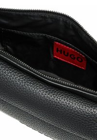 Schwarze Clutch aus strukturiertem Leder mit Reißverschluss, innen mit einem roten "HUGO"-Etikett. Glattes schwarzes Innenfutter.