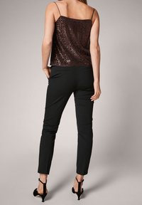 Top burdeos con lentejuelas y tirantes finos, combinado con pantalones negros ajustados y tacones negros con tiras. Textura suave y silueta ajustada.