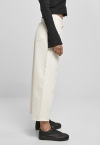 Breda ben, off-white denimbyxor med en mjuk textur. Matchas med en svart, ribbad topp med utställda ärmar. Svarta sneakers fulländar looken.