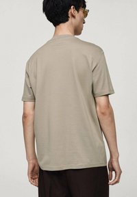 T-shirt in cotone beige con maniche corte, orlo dritto e una texture liscia. Nessun motivo o grafica visibili. Design semplice.