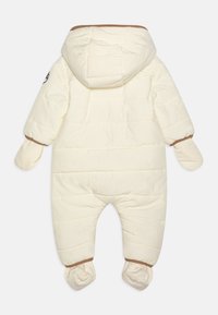 Tuta imbottita color bianco sporco con cappuccio, rifiniture marroni a contrasto e muffole e scarpine integrate. Texture trapuntata a rombi su tutta la superficie.