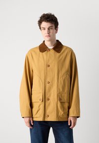 Giacca in tela gialla con colletto in corduroy marrone, dotata di chiusura con bottoni, due tasche frontali e vestibilità rilassata.