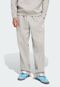Light grey sweatpants in a relaxed fit with an elastic waistband. Features an Adidas logo in white. Paired with blue athletic shoes.