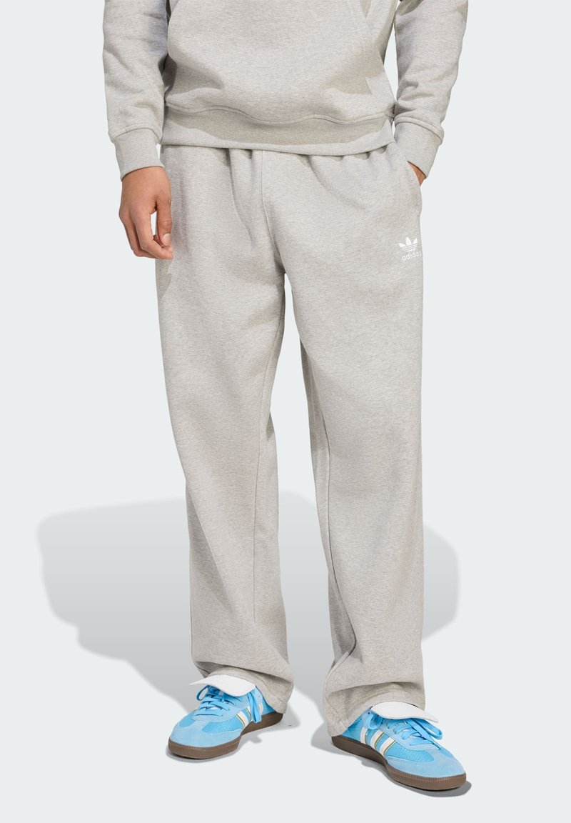 Light grey sweatpants in a relaxed fit with an elastic waistband. Features an Adidas logo in white. Paired with blue athletic shoes.