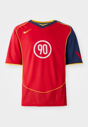 Le maillot de sport rouge présente des manches courtes et un col en V. Le design inclut des accents bleus, un piping jaune et un logo circulaire blanc avec "90".
