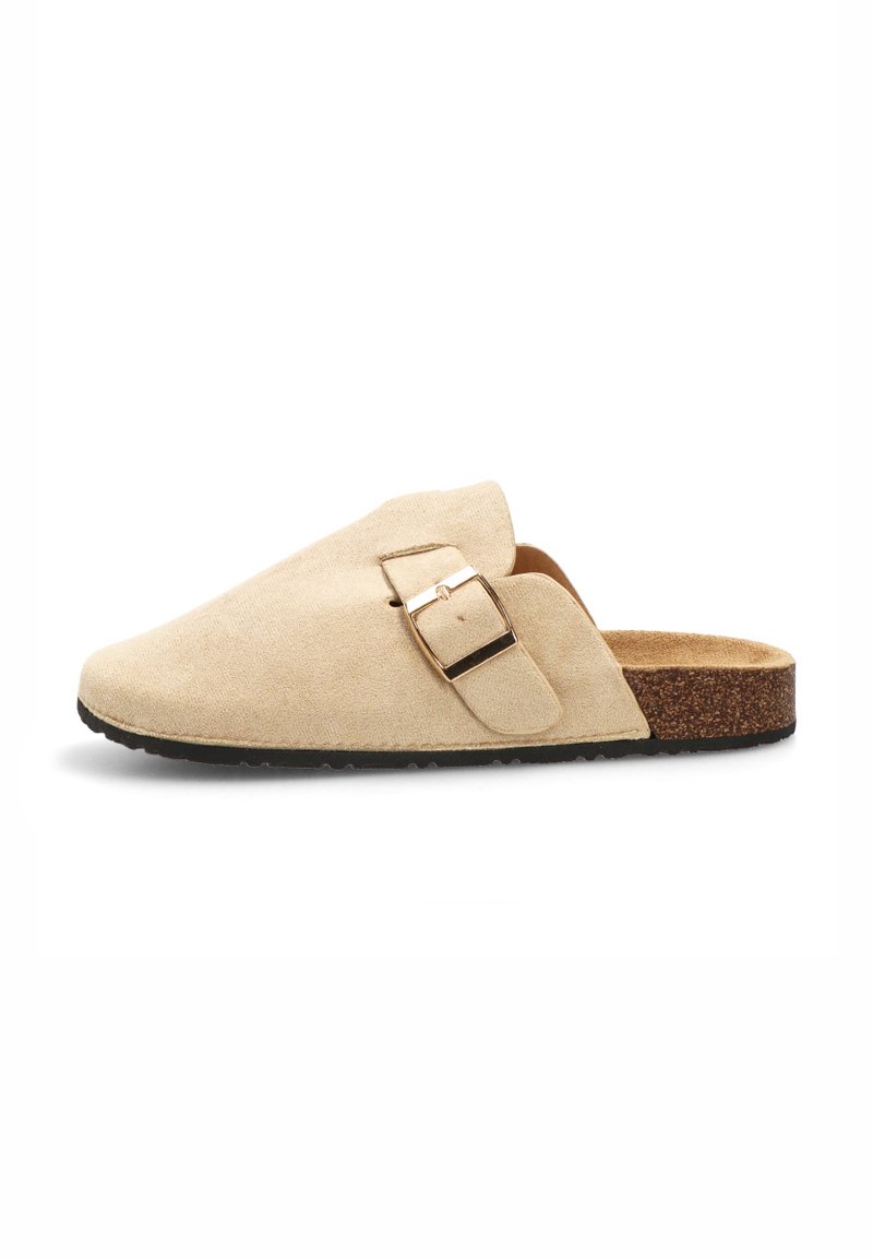 Zapato de ante beige tipo slip-on con suela de corcho plana, que presenta un detalle de hebilla lateral y una textura suave. Diseño simple sin patrones.