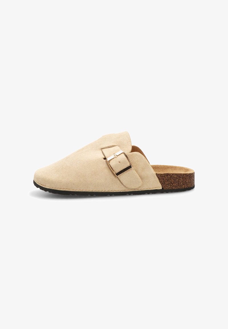 Zapato de ante beige tipo slip-on con suela de corcho plana, que presenta un detalle de hebilla lateral y una textura suave. Diseño simple sin patrones.