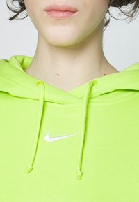 Ljus limegrön huvtröja med dragsko, prydd med en liten vit Nike-logotyp på bröstet. Tillverkad av mjukt tyg med slät yta.