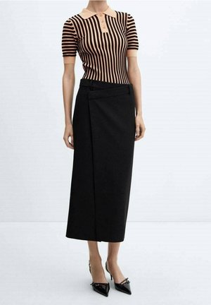 Femme portant un polo à manches courtes rayé beige et noir, une jupe midi portefeuille noire et des talons noirs pointus.