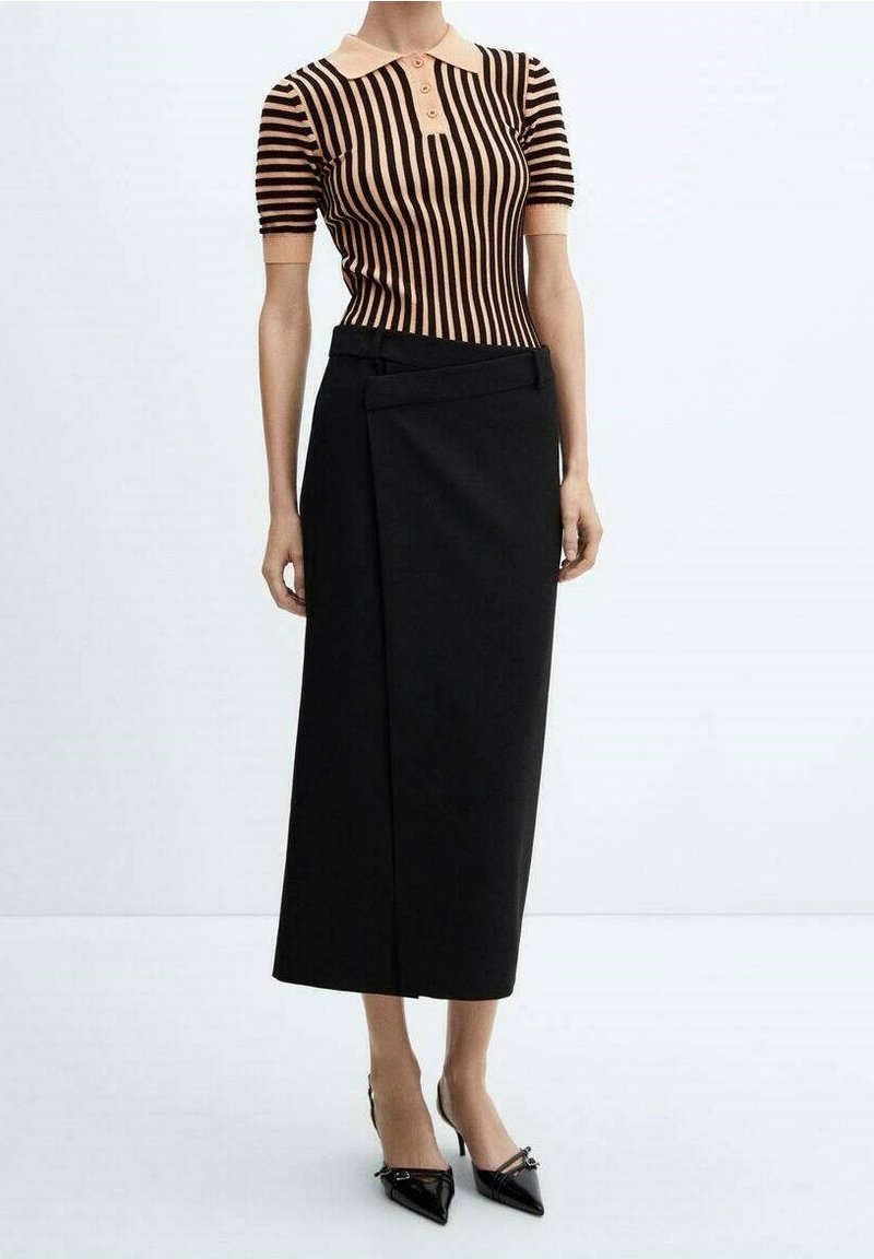 Femme portant un polo à manches courtes rayé beige et noir, une jupe midi portefeuille noire et des talons noirs pointus.