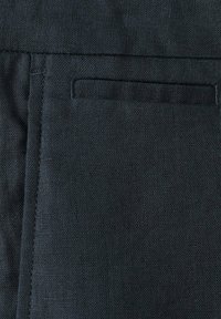 Gros plan d'un tissu foncé avec une poche horizontale fendue et des coutures visibles le long des bords.