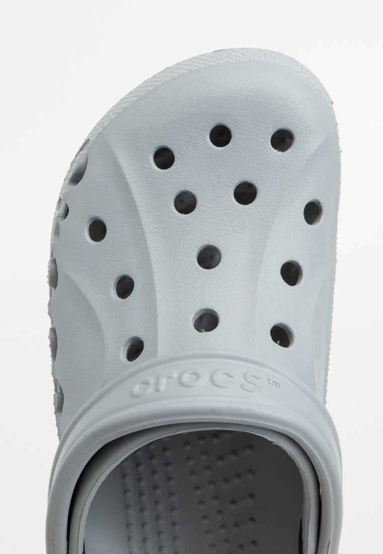 Zuecos Crocs de color gris claro con una superficie texturizada, que cuentan con múltiples agujeros de ventilación y una suela gruesa y redondeada para mayor comodidad.