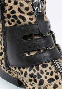 Leopard print ankle boot with black leather straps and zipper details. The upper is textured and features cutouts for added design elements.