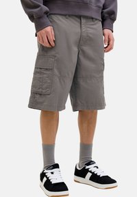 Gray cargo shorts with multiple side pockets, a relaxed fit, and stitched detailing. Paired with black sneakers and gray socks.