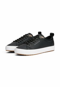 Schwarze Leder-Sneaker mit weißen Gummisohlen, runden Schnürsenkeln und einem kleinen Logo-Patch an der Seite. Texturiertes Obermaterial und langlebiges Design.