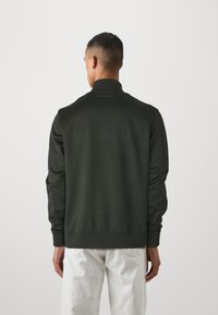 Sweatshirt verde escuro com um colarinho alto, punhos e barra canelados. Apresenta um design minimalista com um logotipo subtil nas costas.