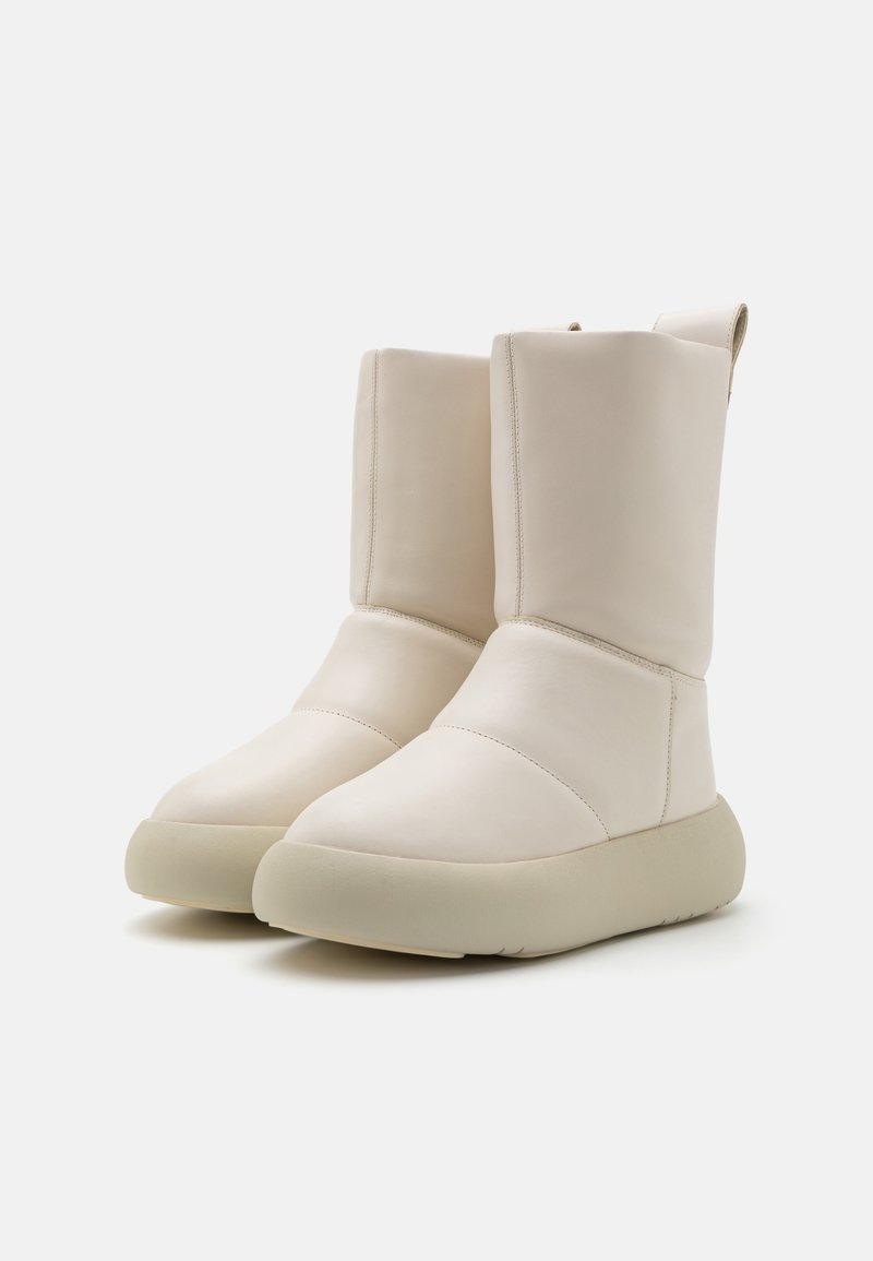 Stivaletti alla caviglia impermeabili di colore crema con tomaia in pelle liscia, punta arrotondata e suola in gomma spessa. Presentano dettagli di cucitura minimalisti.