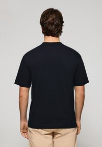 Svart kortärmad T-shirt, tillverkad av bomull, med rundad halsringning och rak nederkant. Inga synliga mönster eller logotyper på baksidan.