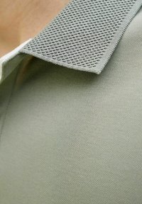 Svetlozelená polo košeľa s textúrovaným, priedušným golierom a hladkou tkaninou na tele, prezentujúca jednoduchý dizajn a čisté línie.