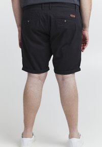 Pantalones cortos de algodón negros con un dobladillo enrollado, dos bolsillos traseros y un branding sutil. Combinados con zapatillas blancas, con una textura suave.