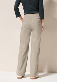 Beige, lichtgewicht, brede broek met een elastische tailleband, voorzien van twee achterzakken en een soepele textuur, gecombineerd met witte schoenen.