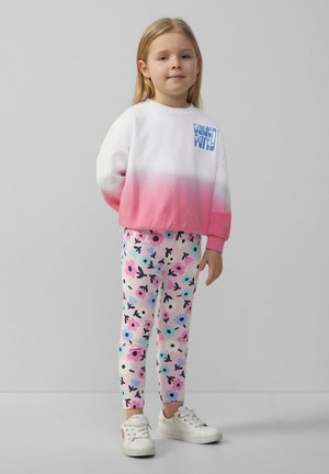Bluza w białym kolorze przechodzącym w różowy z grafiką "Garden Party"; legginsy w kwiatowy wzór w różowym, niebieskim i czarnym kolorze; białe sneakersy.