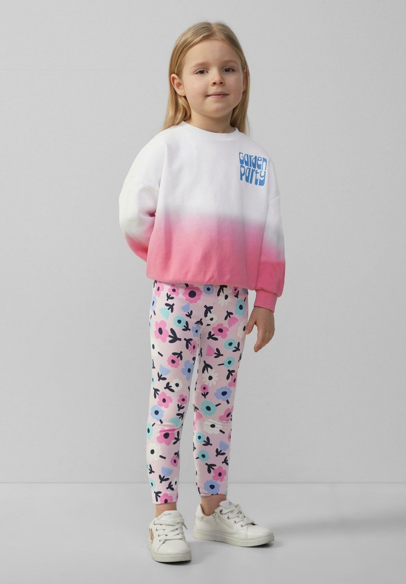 Bluza w białym kolorze przechodzącym w różowy z grafiką "Garden Party"; legginsy w kwiatowy wzór w różowym, niebieskim i czarnym kolorze; białe sneakersy.