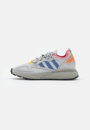 Szary sportowy sneaker z niebieskimi paskami, różową podszewką wewnętrzną, pomarańczowym detalem na pięcie, żółtą pętlą na sznurówki i amortyzowaną podeszwą na białym tle.