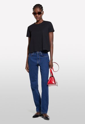 T-shirt noir court, jean droit bleu, ballerines noires et un petit sac à main rouge. Accessoirisé avec des lunettes de soleil teintées brunes.