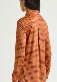 Camicia a maniche lunghe in tessuto arancione con pois viola, con collo a risvolto, polsini con bottoni e dettaglio plissettato sul retro.