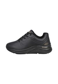Zapatilla negra con una parte superior sintética texturizada, suela acolchada y un diseño elevado. Presenta cordones negros y un acento dorado de "Arch Comfort".