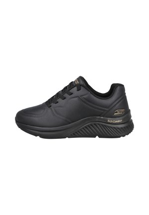 Zapatilla negra con una parte superior sintética texturizada, suela acolchada y un diseño elevado. Presenta cordones negros y un acento dorado de "Arch Comfort".