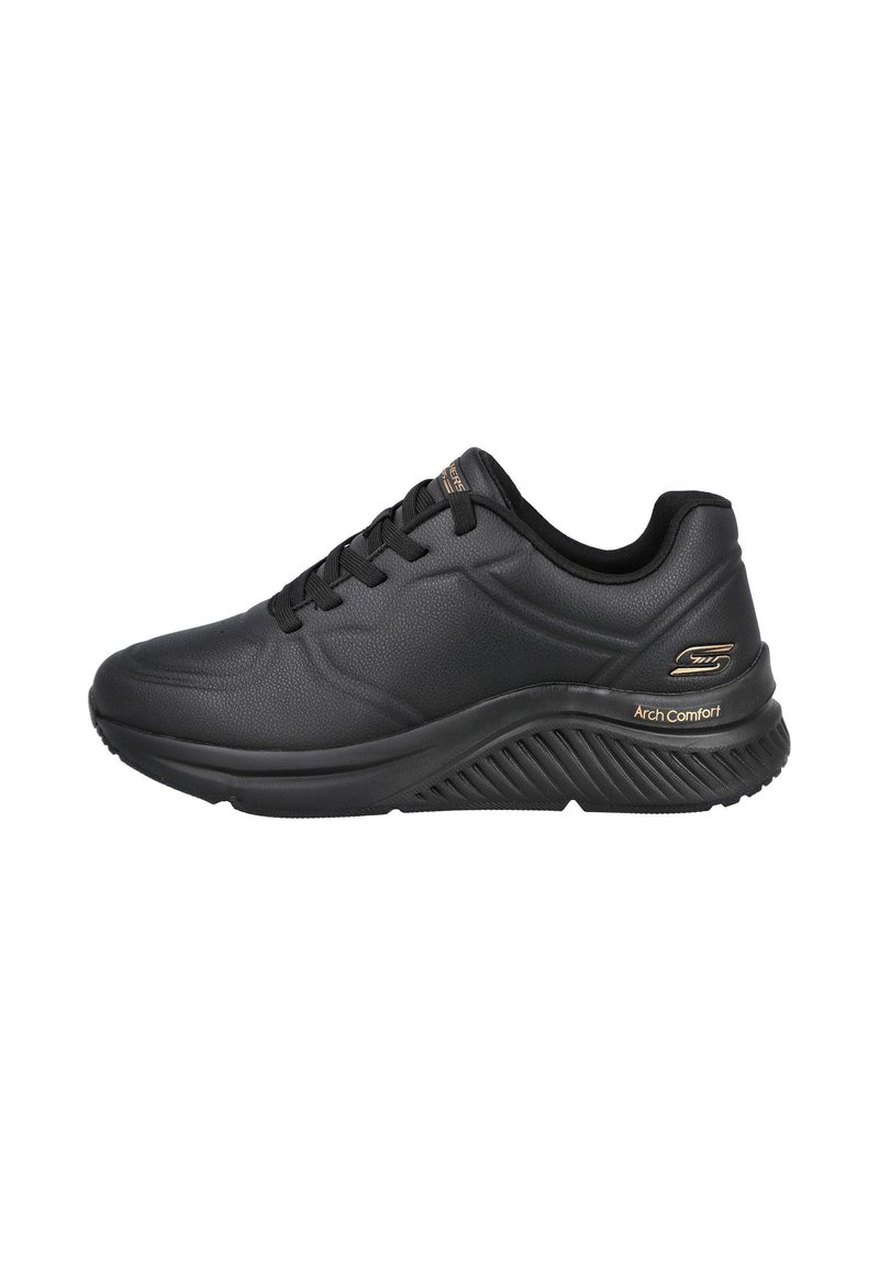 Zapatilla negra con una parte superior sintética texturizada, suela acolchada y un diseño elevado. Presenta cordones negros y un acento dorado de "Arch Comfort".