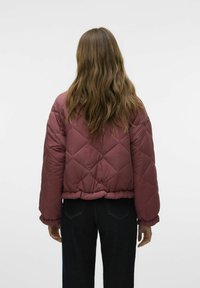 Giacca invernale trapuntata bordeaux con design corto, orlo elasticizzato e maniche voluminose. Indossata sopra jeans scuri, vista da dietro.