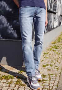 Világoskék farmernadrág, egyenes szabású, szürke és fehér tornacipőkkel párosítva, amelyek különböző textúrájú anyagból és gumitalpból készültek.