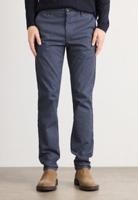 Mornarsko modri slim-fit hlače iz teksturirane tkanine, ki vključujejo sprednje žepke, zadrgo in en gumb za zapiranje. Ustrezajo s svetlobo rjavimi gležnjarji.