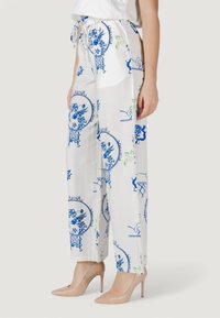 Pantaloni a gamba larga bianchi con motivo floreale dai disegni blu e verdi, dotati di cintura elastica e fiocco, abbinati a tacchi alti color nude.