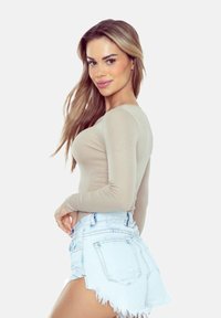 Beżowa bluzka z długim rękawem w połączeniu z jasnoniebieskimi szortami dżinsowymi z przetarciami, o dopasowanej konstrukcji i prążkowanej teksturze.